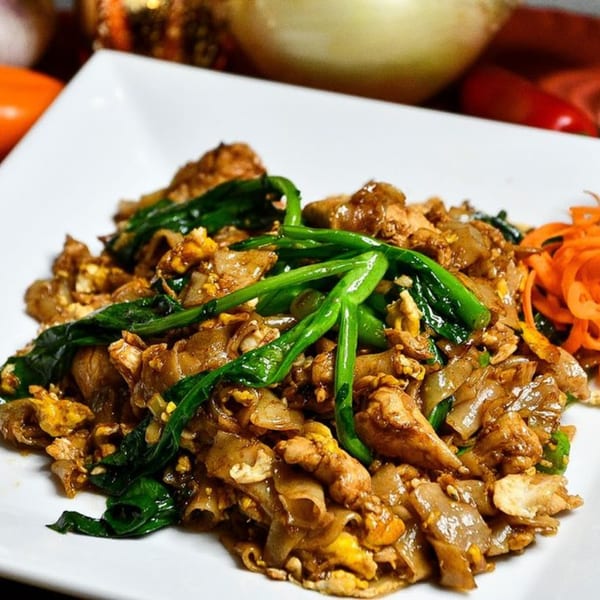 Pad See Ew with wide rice noodles, chicken, Chinese broccoli, and scrambled egg on a white plate.