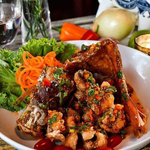 Crispy fried fish with sweet chili sauce, garnished with lettuce, carrots, and cherry tomatoes.