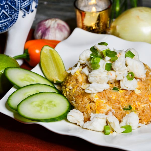 Crab fried rice with cucumber slices and lime wedges on a white plate, with ingredients in the background.