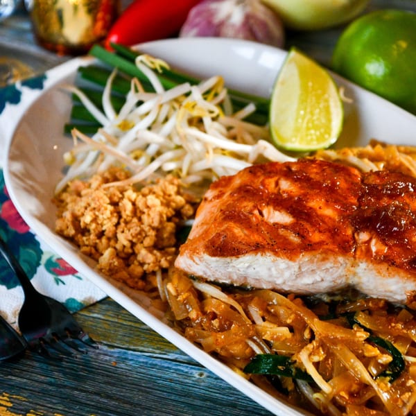Salmon Pad Thai with bean sprouts, crushed peanuts, and a lime wedge on a white plate.