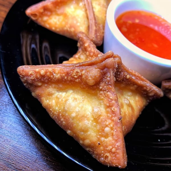 Golden-brown crab rangoon appetizers on a black plate, with a side of sweet and sour dipping sauce.